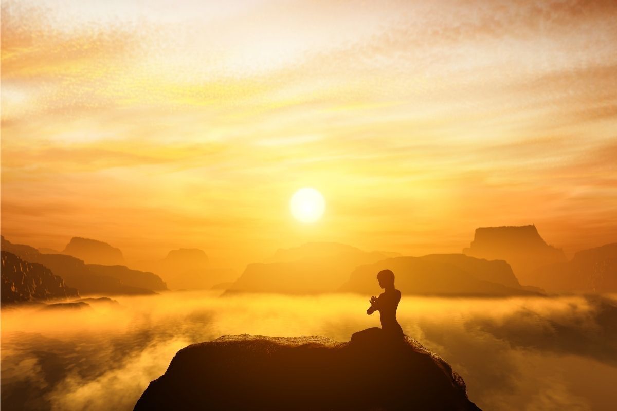 Silhueta de uma pessoa meditando em uma montanha no pôr do sol