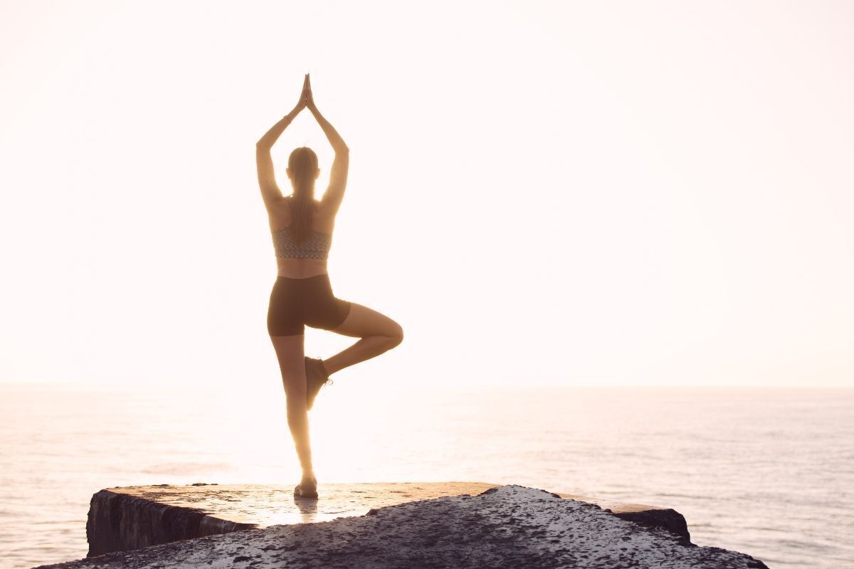 Mulher fazendo uma posição de yoga na frente do mar