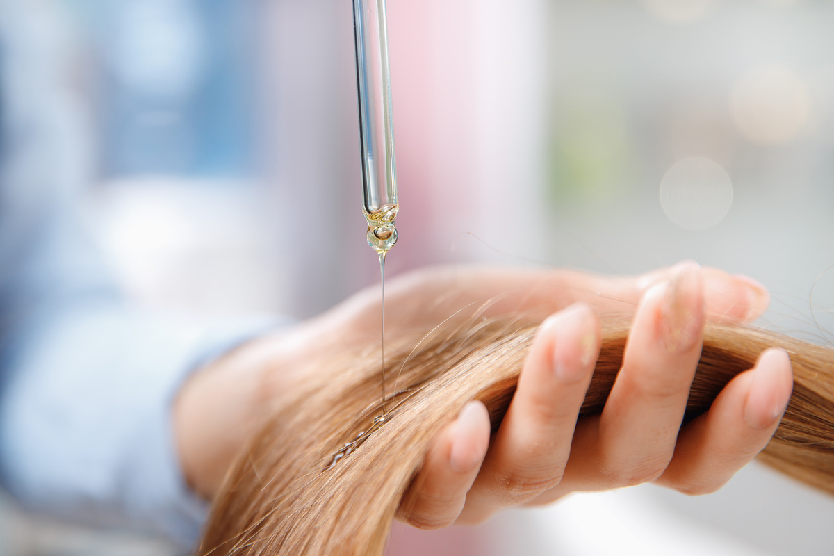 Pessoa aplicando óleo de argan no cabelo com conta gotas
