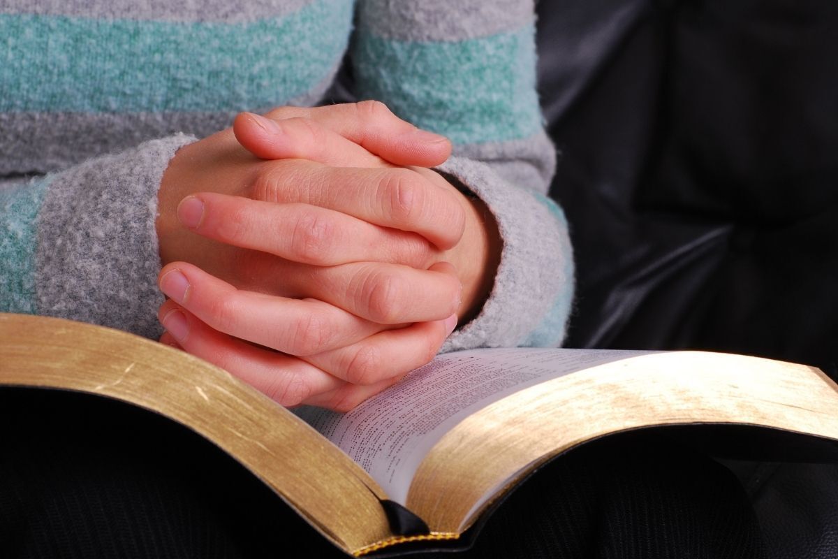 Mãos de uma pessoa rezando sob a bíblia