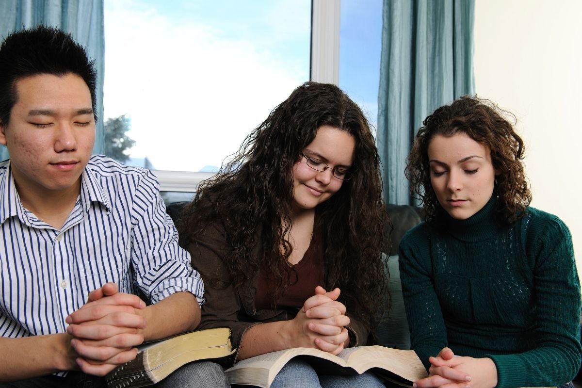 Um homem e duas mulheres estão lendo a Bíblia Sagrada juntos e rezando
