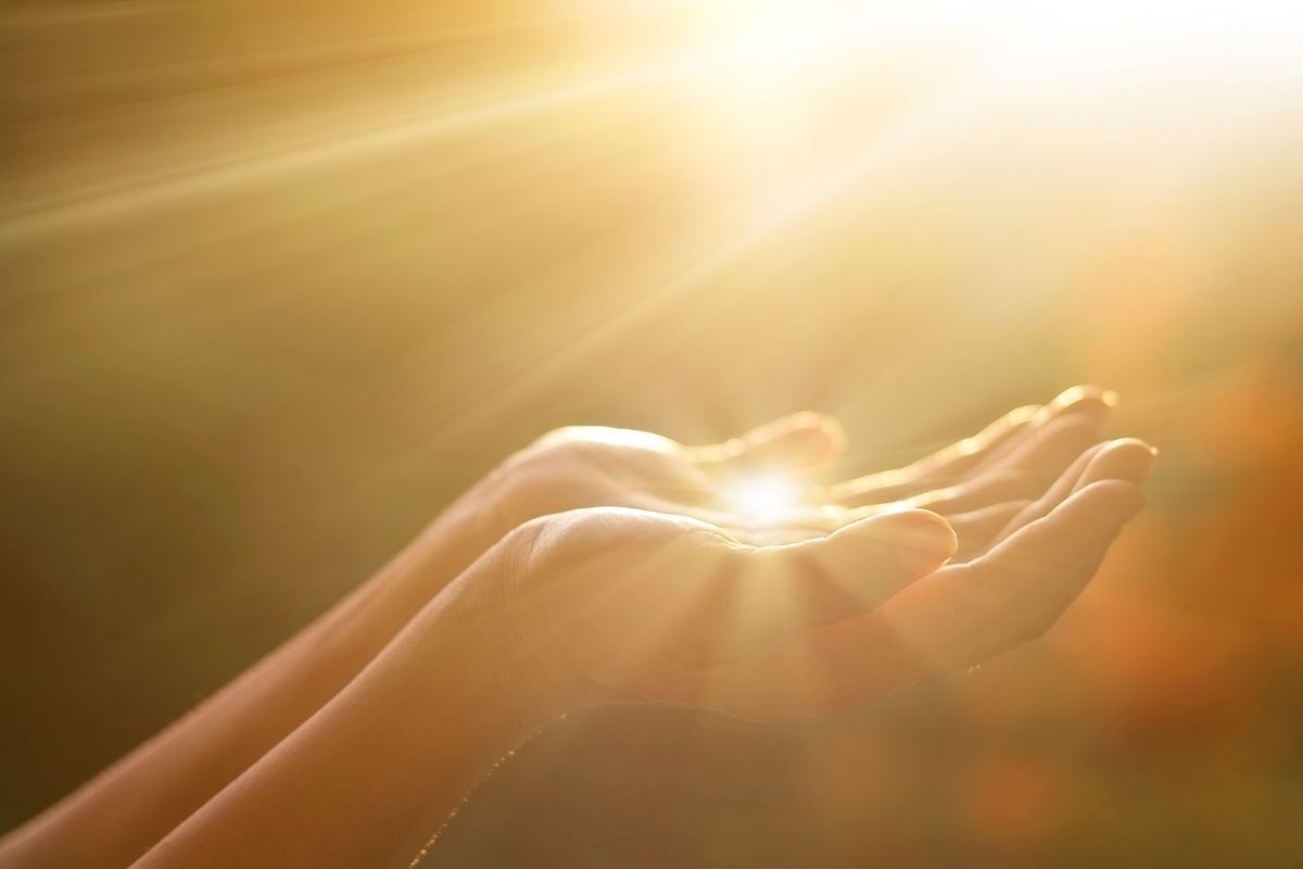 Mãos de uma pessoa em formato de oração iluminadas por uma luz