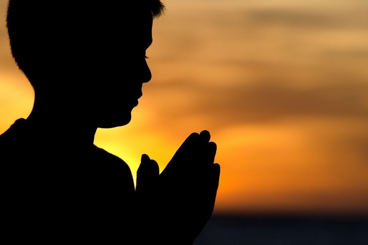 Silhueta de uma pessoa rezando em um pôr do sol