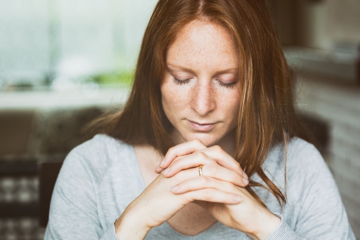 Mulher rezando com os olhos fechados