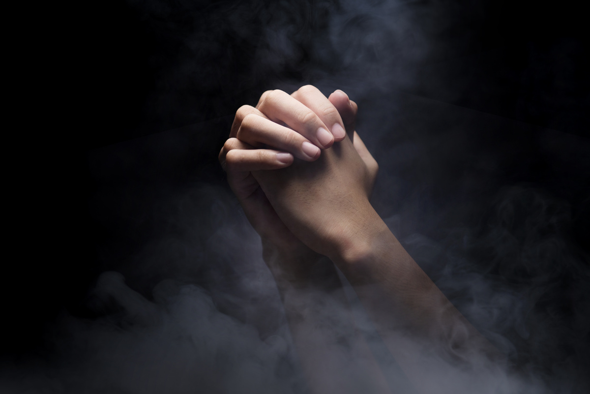 Mãos em posição de oração em fundo preto com névoa ao redor