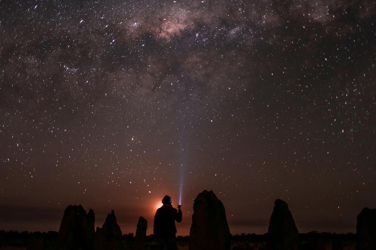 Pessoa com uma lanterna olhando para o céu estrelado. 