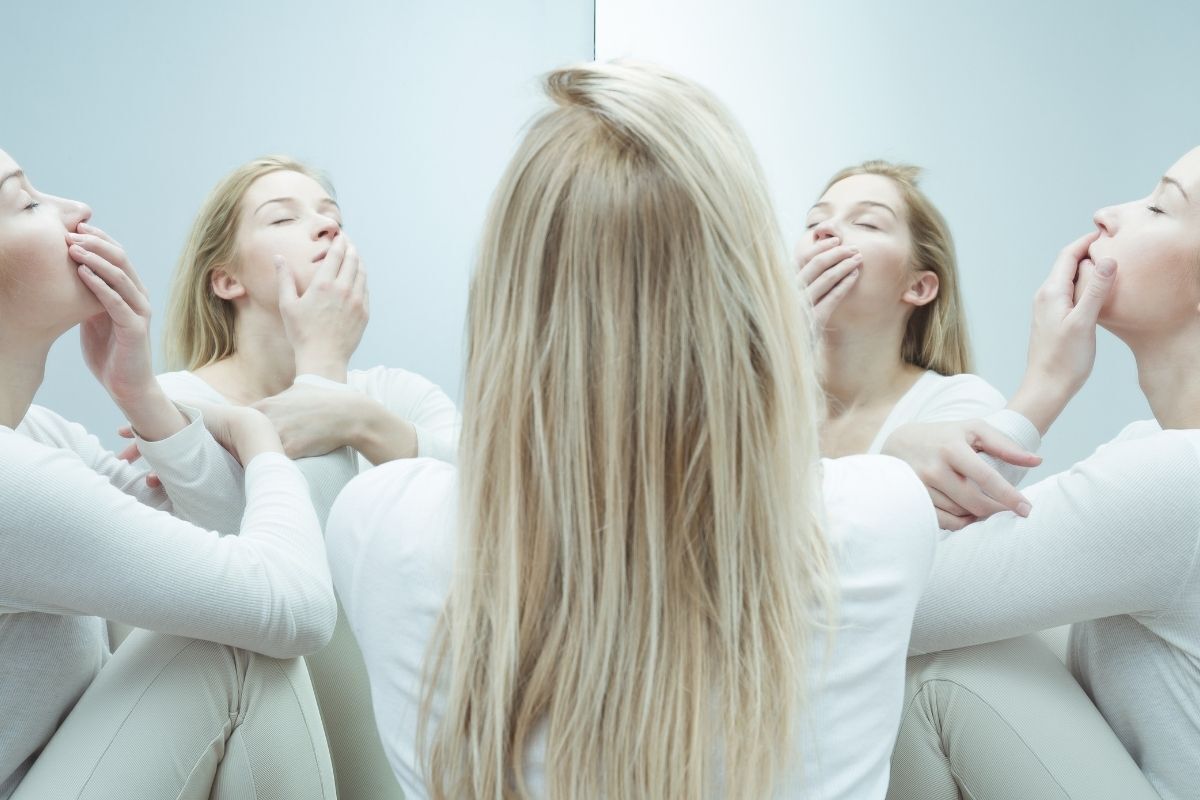 Imagem de uma mulher sentada em um espelho com vários reflexos