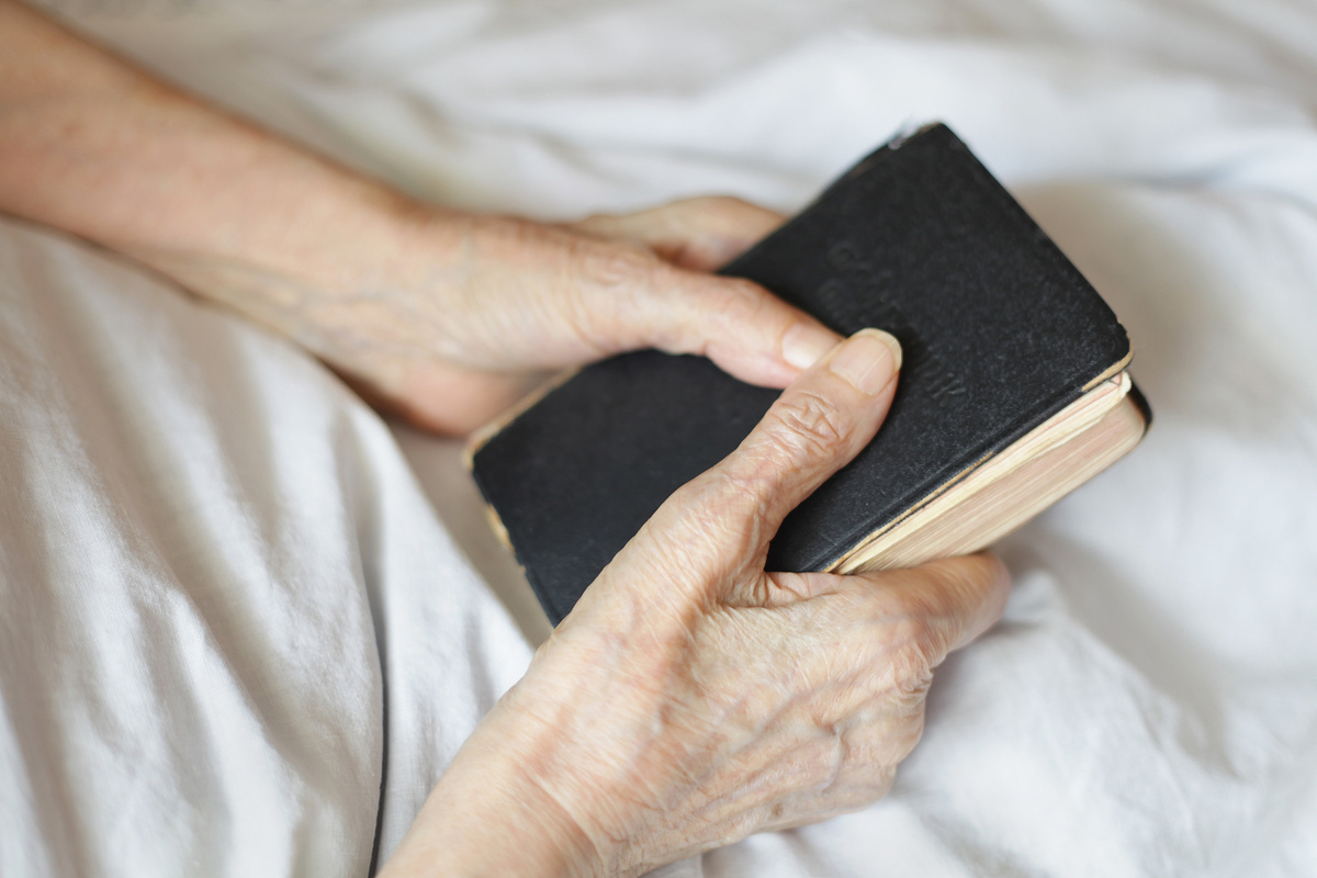 Mãos segurando uma Bíblia na cama