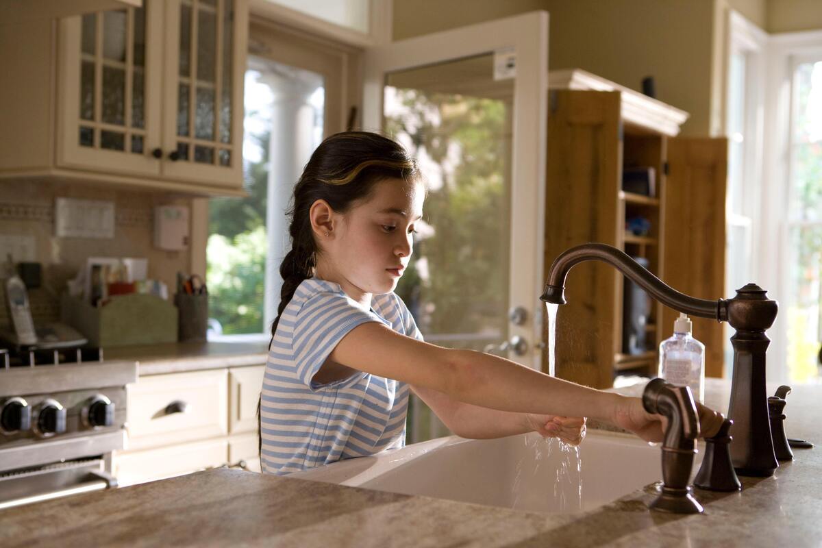 Criança lavando as mãos em torneira da cozinha