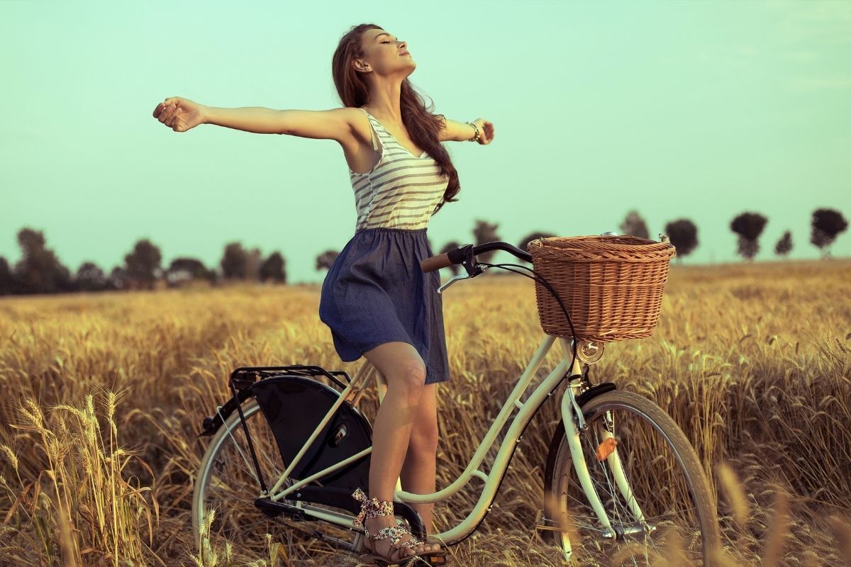 Mulher com uma bicileta no campo, com os braços abertos representando sua liberdade