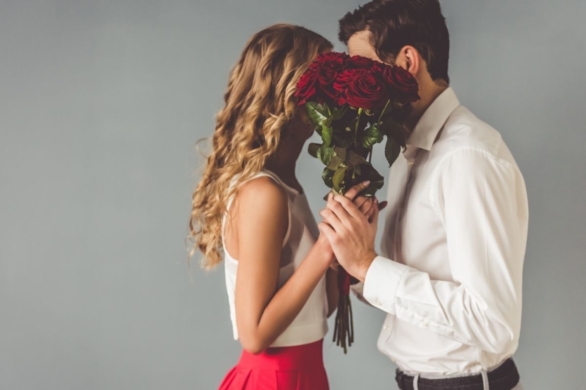 Casal escondendo o beijo com um buquê de rosas vermelhas