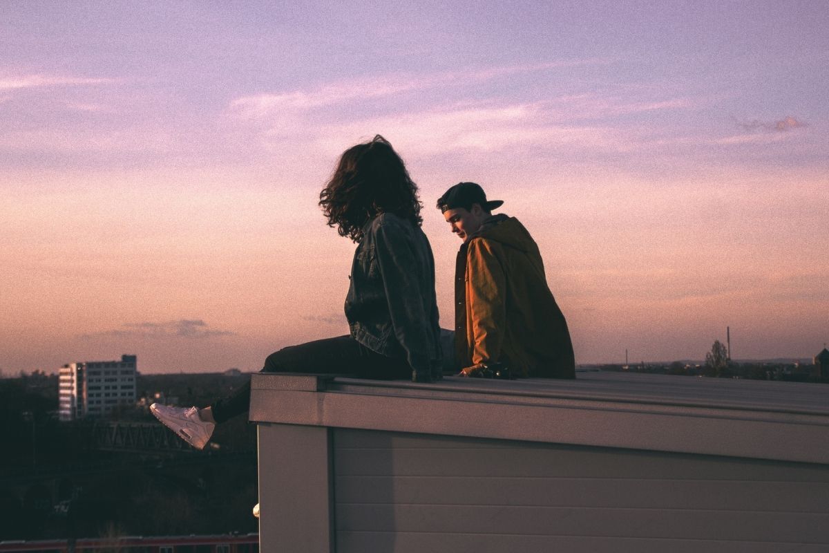 Casal jovem sentado em um telhado no pôr do sol