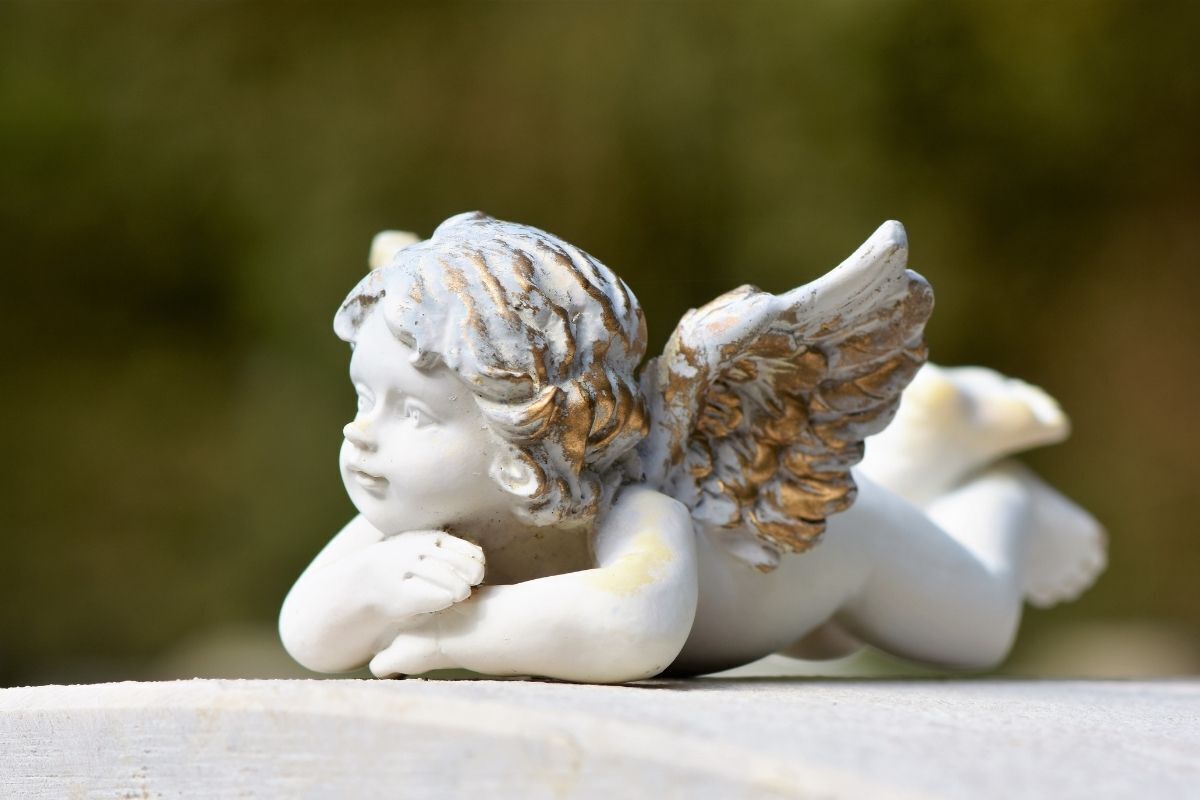 Escultura de anjo deitado com as mãos no queixo