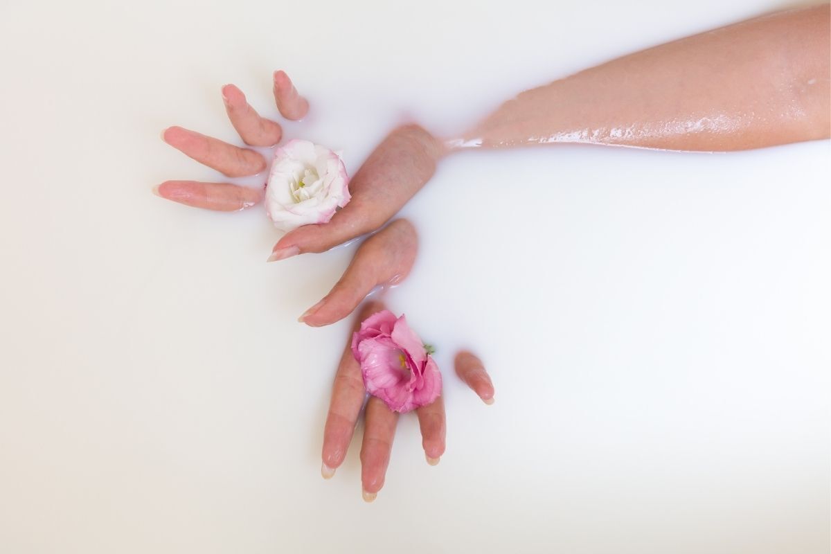 Mulher em uma banheira com leite segurando rosas em suas mãos