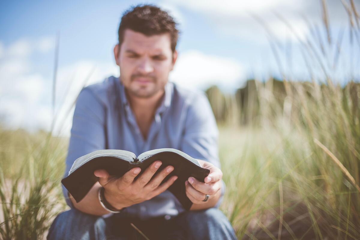 Homem lendo a Bíblia sentado em gramado