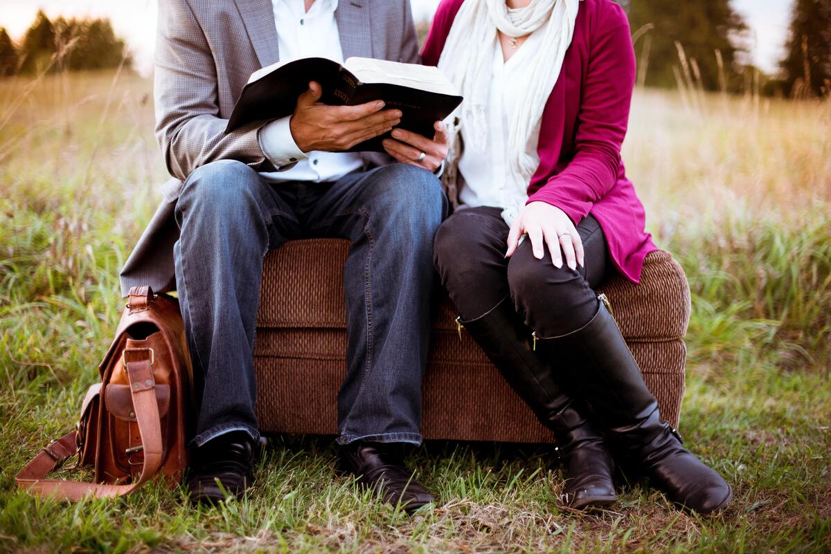 Casal sentado em mala em um gramado lendo a Bíblia