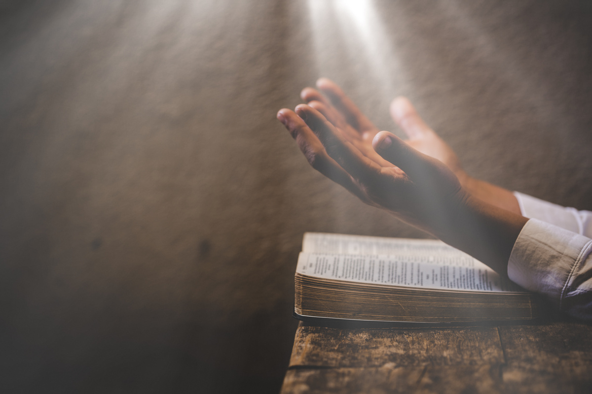 Mãos em sinal de orações sobre Bíblia aberta