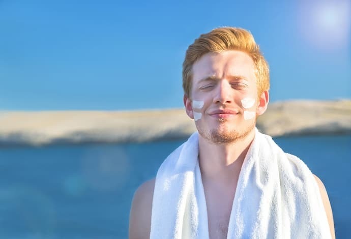 Homem na praia com protetor solar no rosto