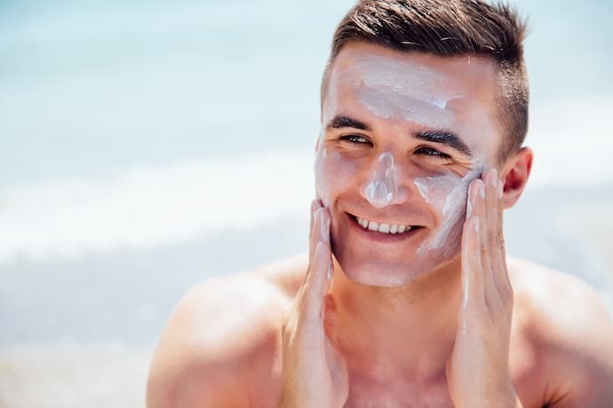 Homem na praia com protetor solar no rosto