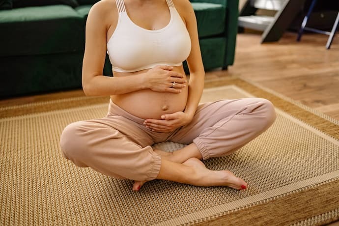 Mulher grávida sentada no chão segurando a barriga