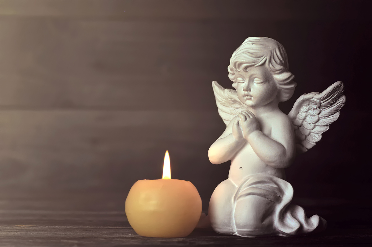 Pequena imagem de anjo rezando ao lado de vela