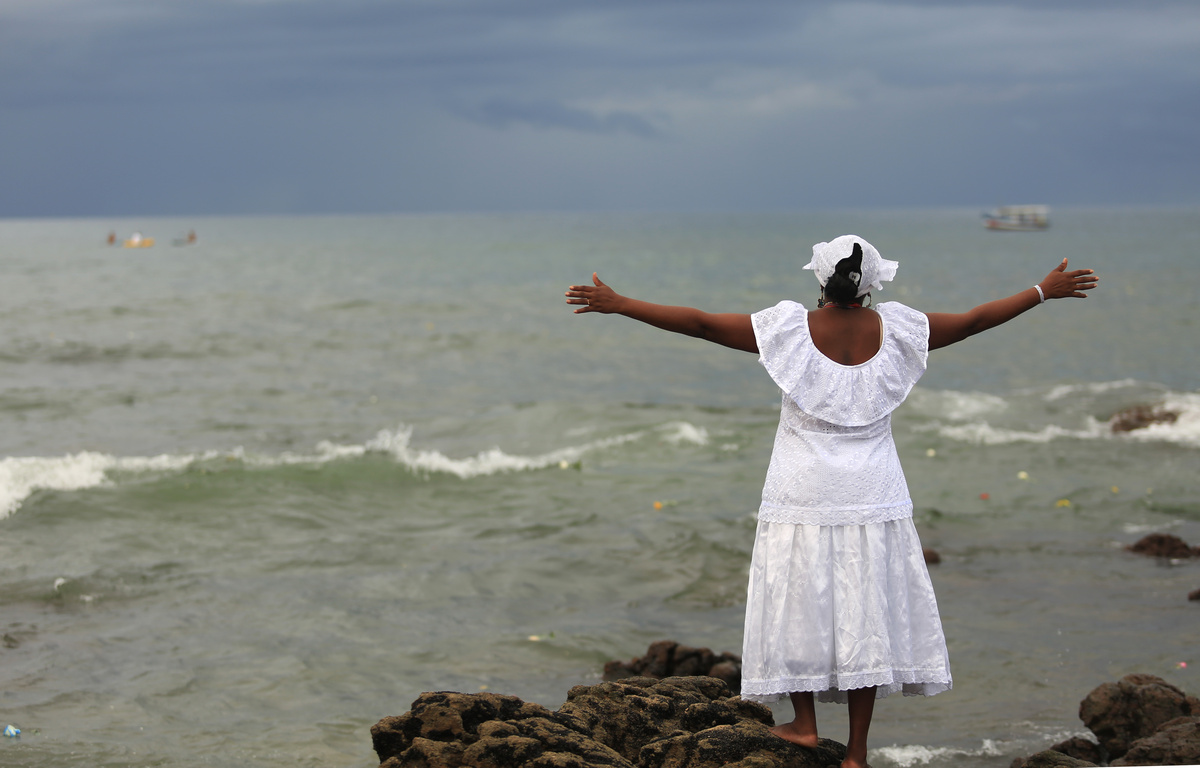Mulher com roupas brancas e braços abertos em direção do mar