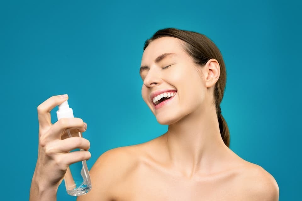 Mulher sorridente aplicando tônico facial spray
