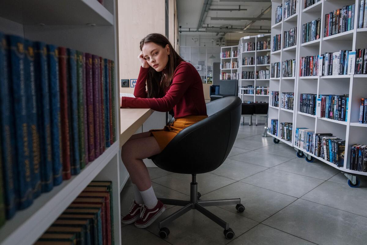 Menina sentada em uma biblioteca procrastinando