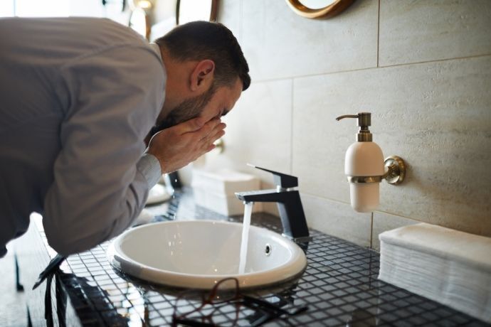 Homem lavando o rosto em pia de banheiro