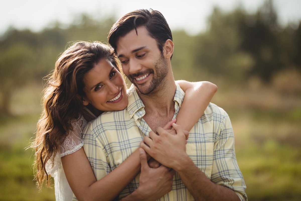 Mulher abraçando homem por trás enquanto ambos sorriem, representando um relacionamento harmonioso entre Câncer e Gêmeos.