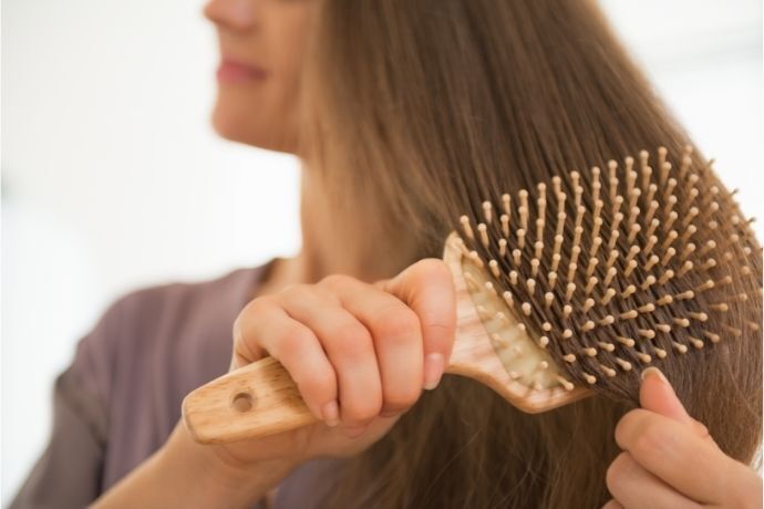 Mulher penteando cabelo com escova de madeira