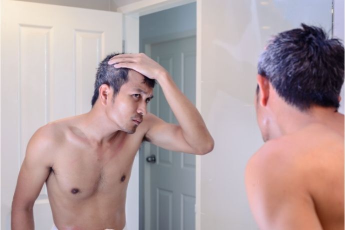 Homem olhando cabelos grisalhos no espelho