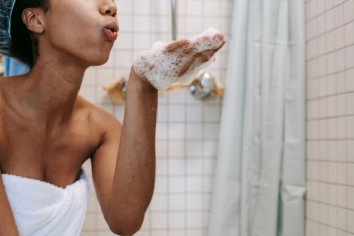 Mulher no banho soprando espuma de shampoo da mão
