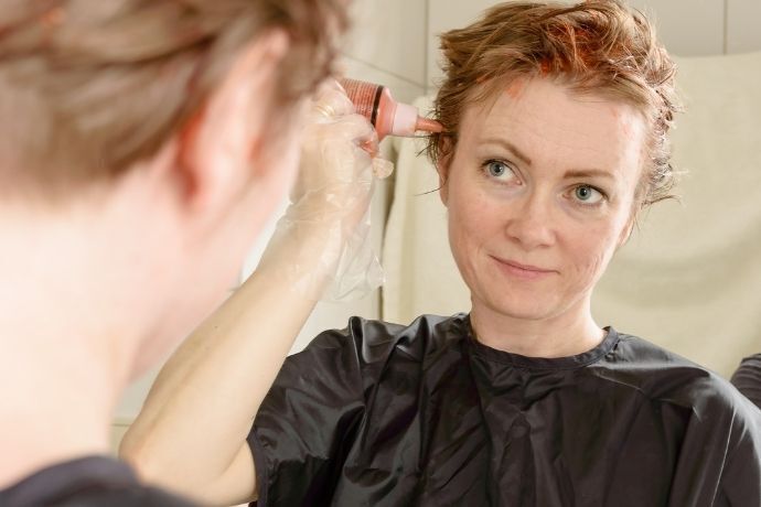 Mulher se olhando no espelho e aplicando tonalizante ruivo no cabelo