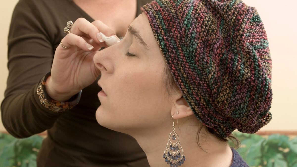 Maquiadora aplicando corretivo no rosto de uma mulher.
