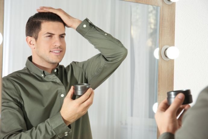 Homem se olhando no espelho e aplicando pomada para o cabelo