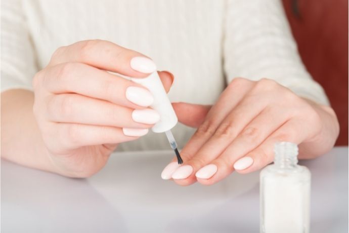 Mulher pintando as unhas com esmalte branco