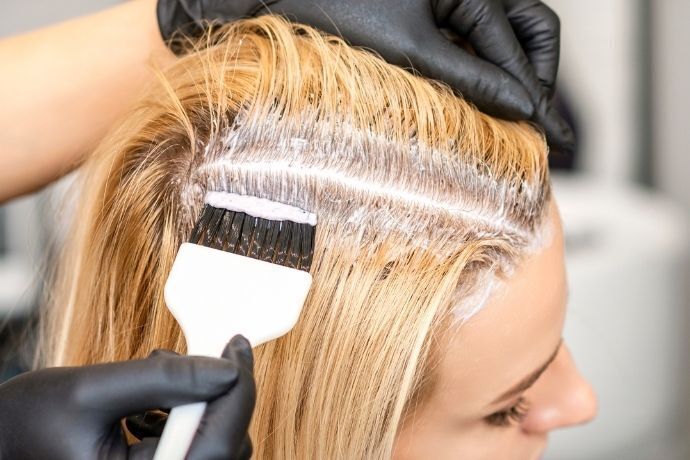 Pessoa aplicando tinta loiro claro em cabelo de mulher