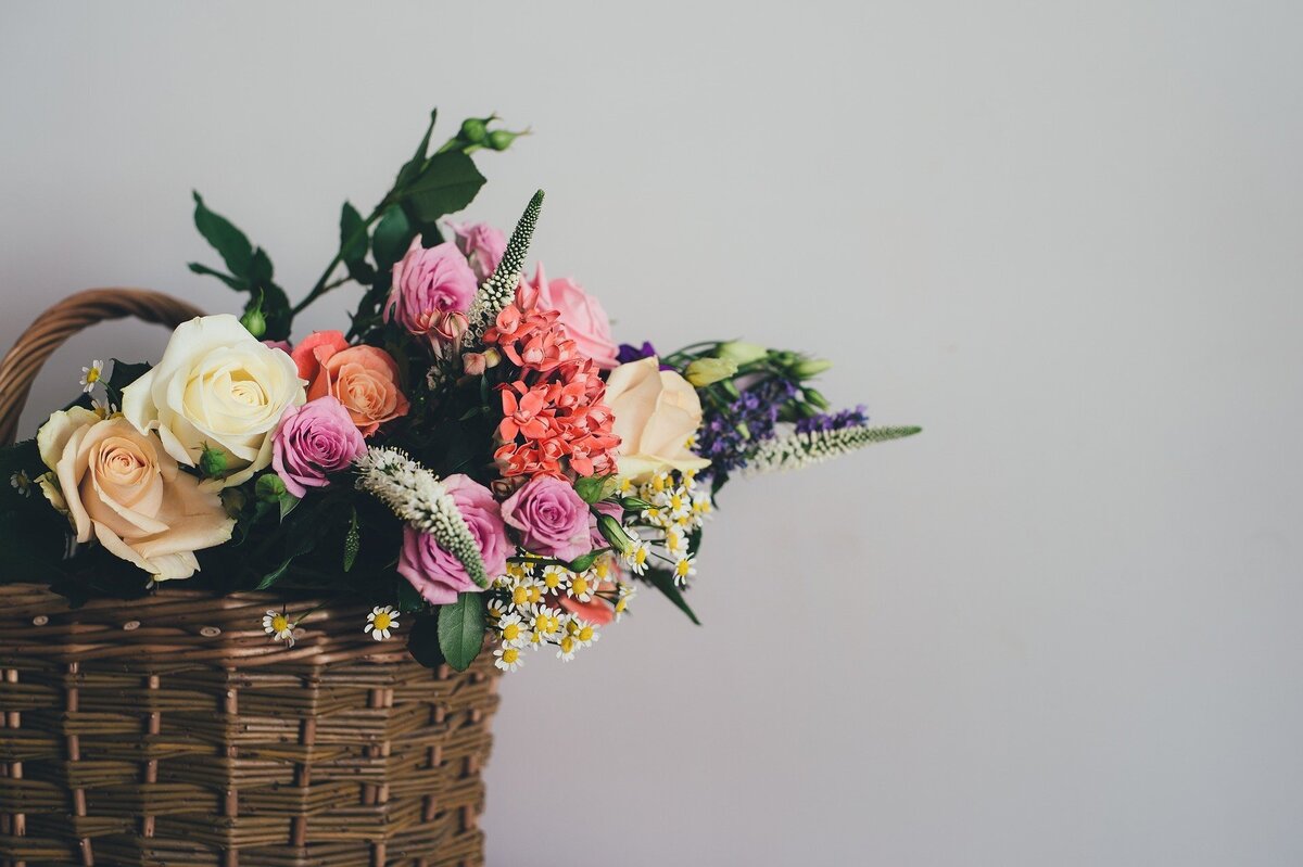 Arranjo floral dentro de cesto marrom, composto por flores rosas e brancas, em meio a cenário branco.