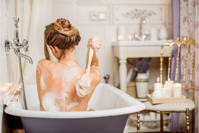 Mulher passando escova nas costas durante banho em banheira