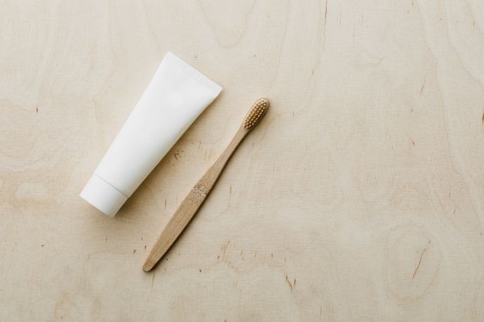 Escova de dente de bambu ao lado de embalagem de creme dental