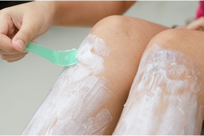 Mulher aplicando creme depilatório na perna com espátula 