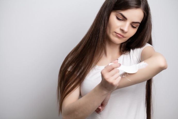 Mulher passando creme depilatório no braço