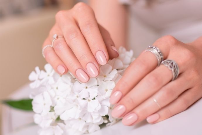 Mãos femininas com unhas pintadas com esmalte claro segurando flores