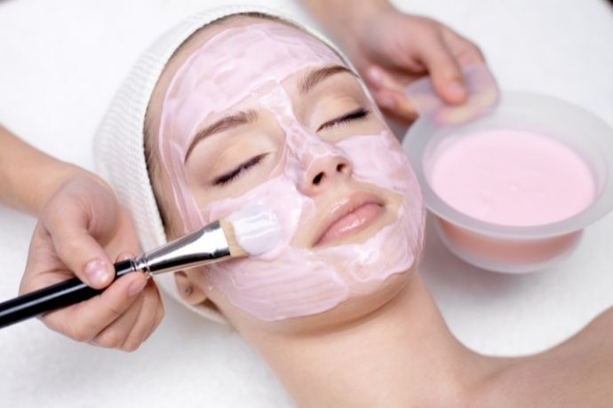 Pessoa aplicando argila rosa no rosto de mulher