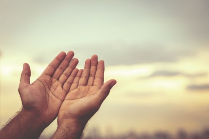 Pessoa com mãos erguidas em direção aos céus em sinal de oração 