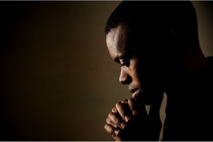Homem rezando em cenário escuro