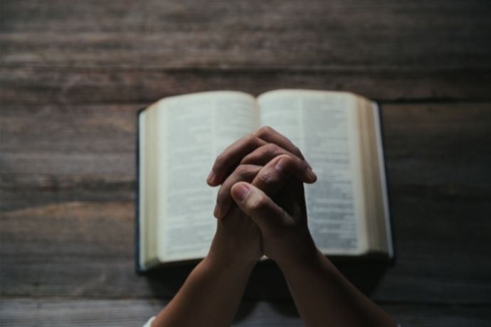 Mãos em sinal de oração em frente a Bíblia