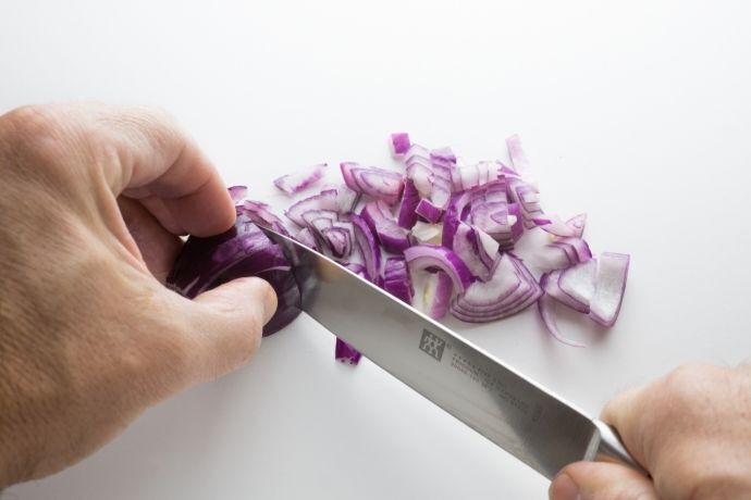 Pessoa cortando cebola roxa com faca