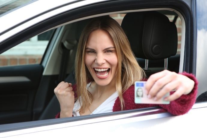 Mulher feliz dentro do carro segurando carteira de motorista